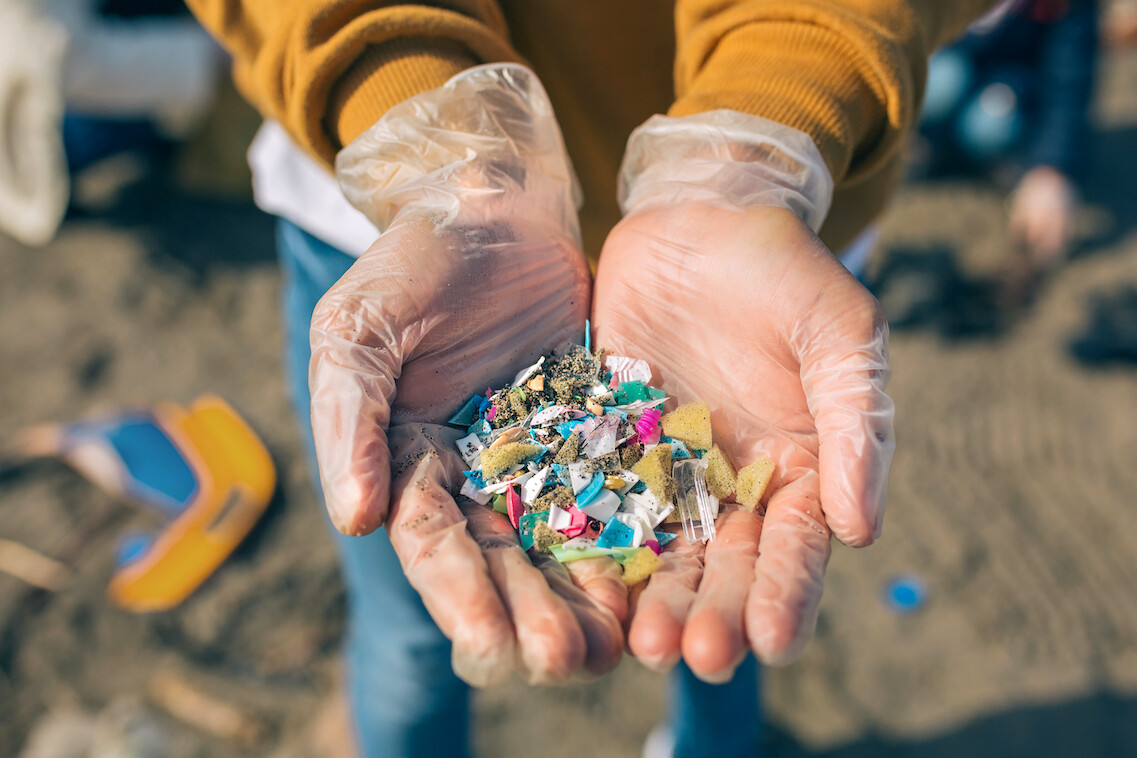Persona muestra en sus manos microplásticos en la playa.